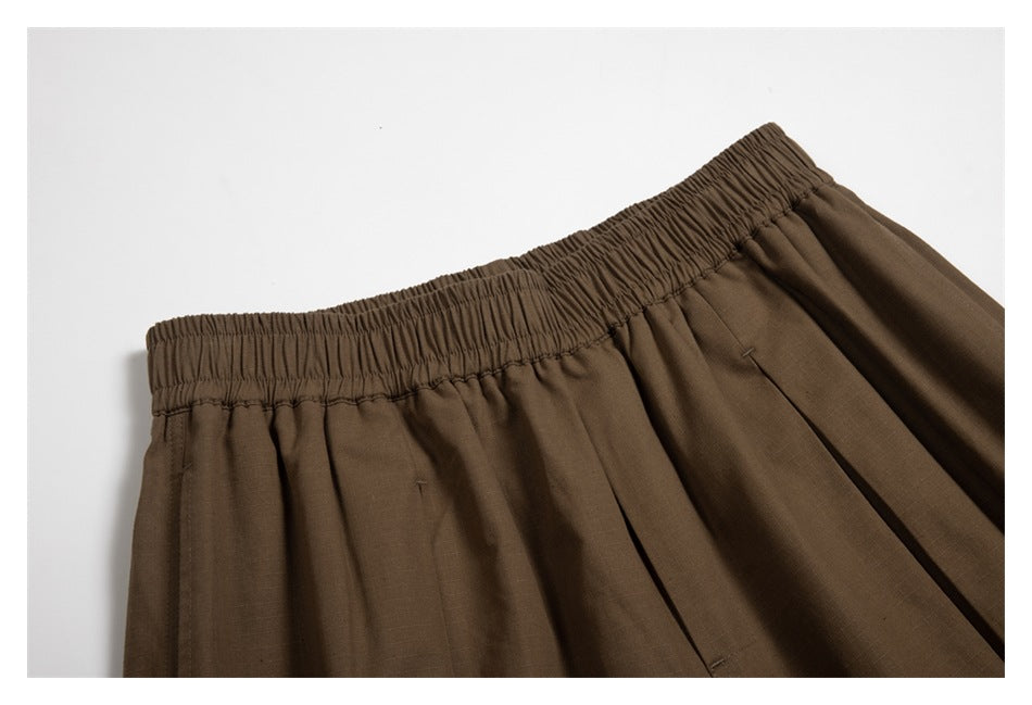 Close-up of brown shorts showing the gathered elastic waistband, stitching, and pleats.