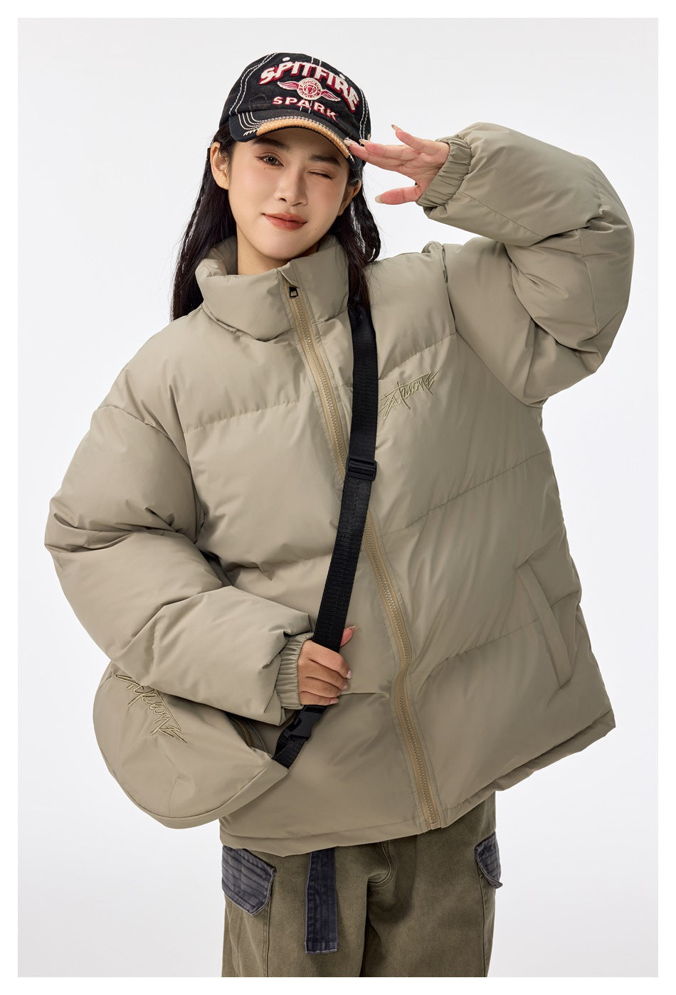 Model wearing a khaki puffer jacket with a black-strap crossbody pouch, with one arm raised