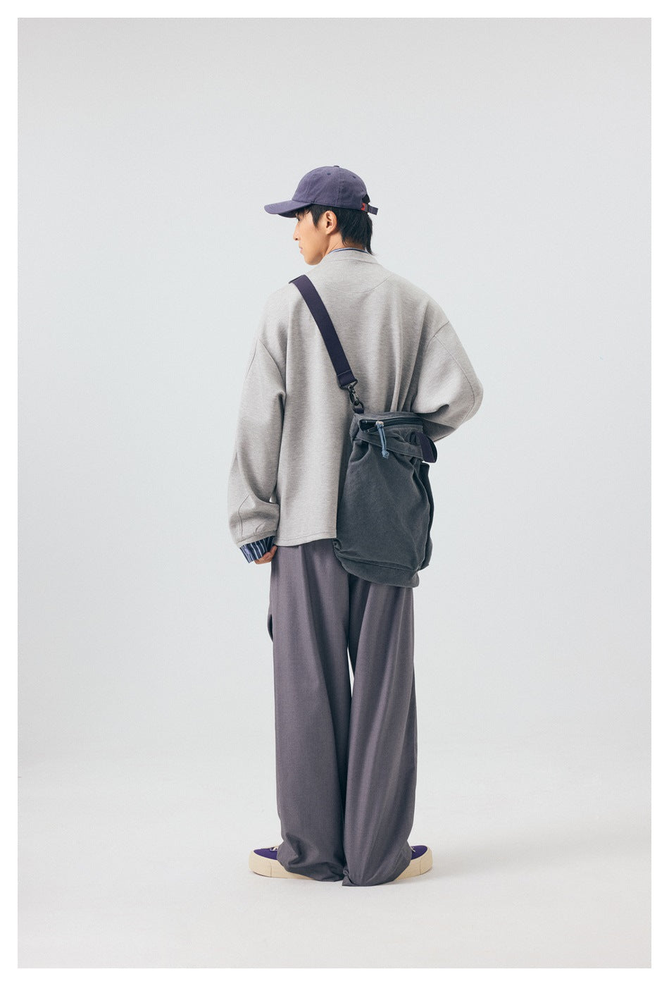 Model seen from the back wearing gray wide-leg trousers with a gray top, cap and shoulder bag