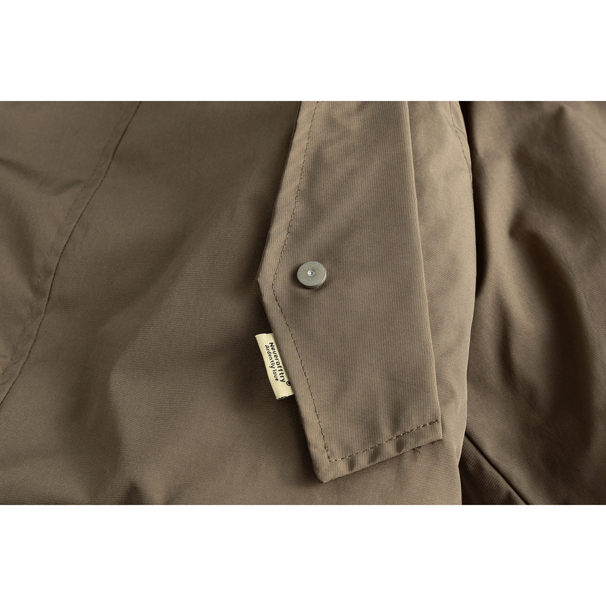 Close-up of an olive-brown jacket showing a flap, snap fastener, stitching, and a small sewn label.