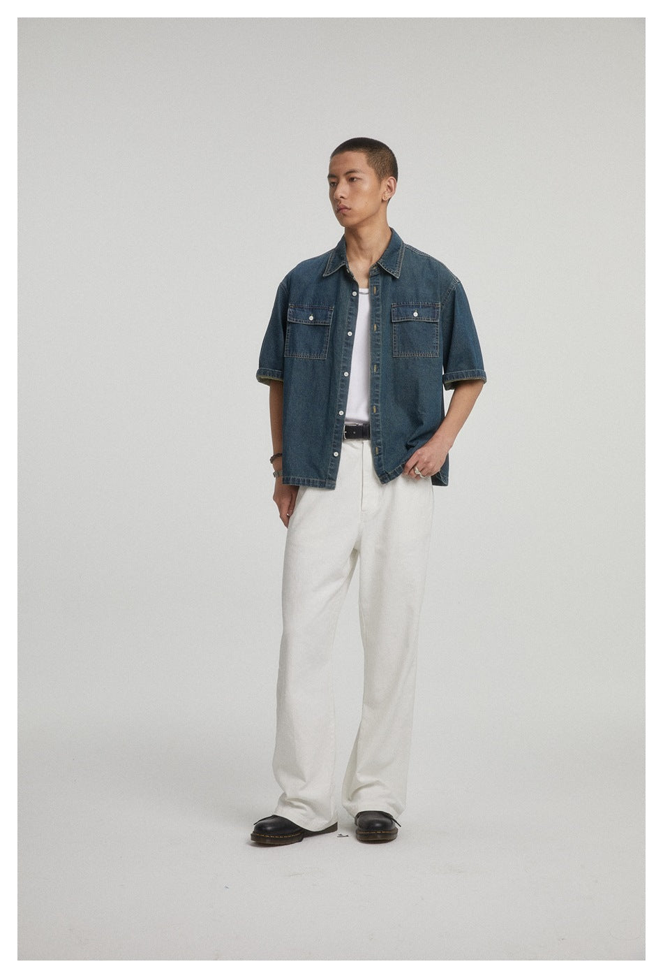 Front view of a model wearing a dark blue short-sleeve denim shirt with two chest pockets over a white tank.