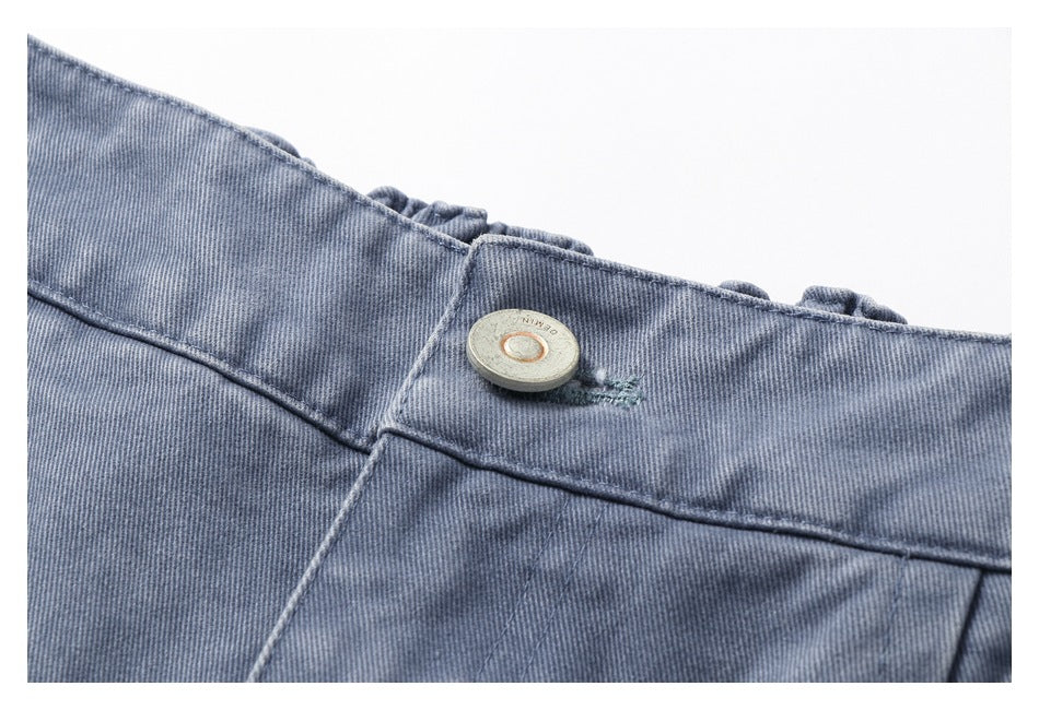 Close-up of a round metal button on the blue-gray trousers' waistband.