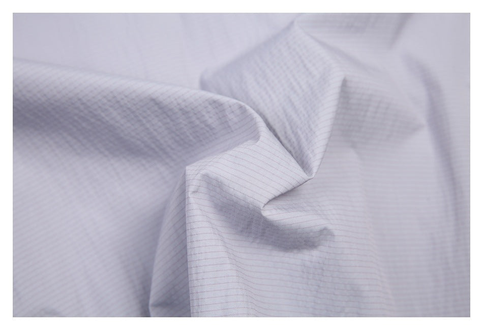 Close-up of pale gray fabric with a fine, subtle grid pattern, draped into soft folds.