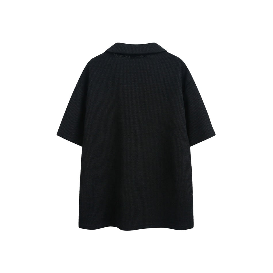Back view of a black short-sleeve textured polo with a folded collar, shown flat on white.