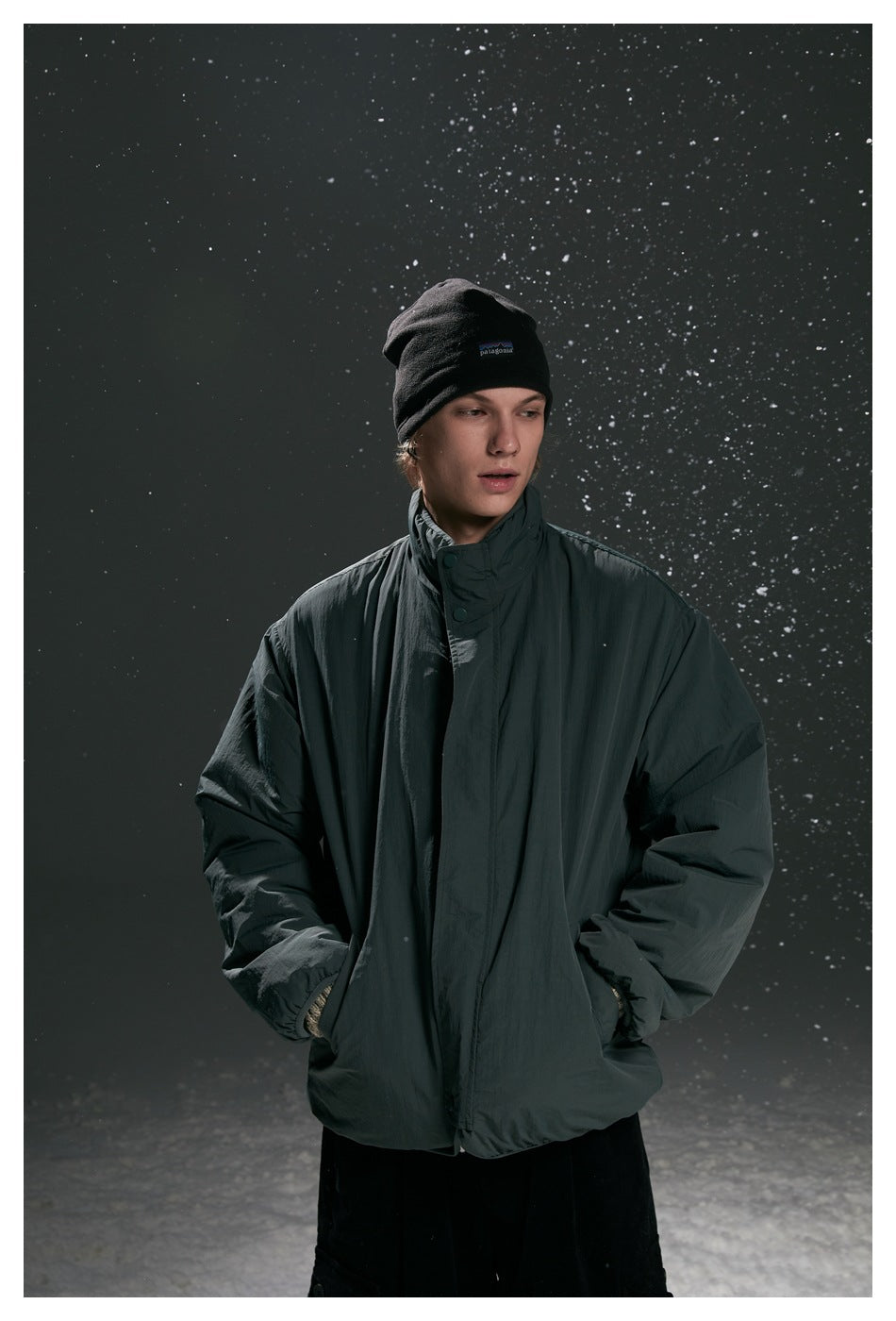 Model wearing a dark charcoal high-collar jacket with front snap closure and black beanie.