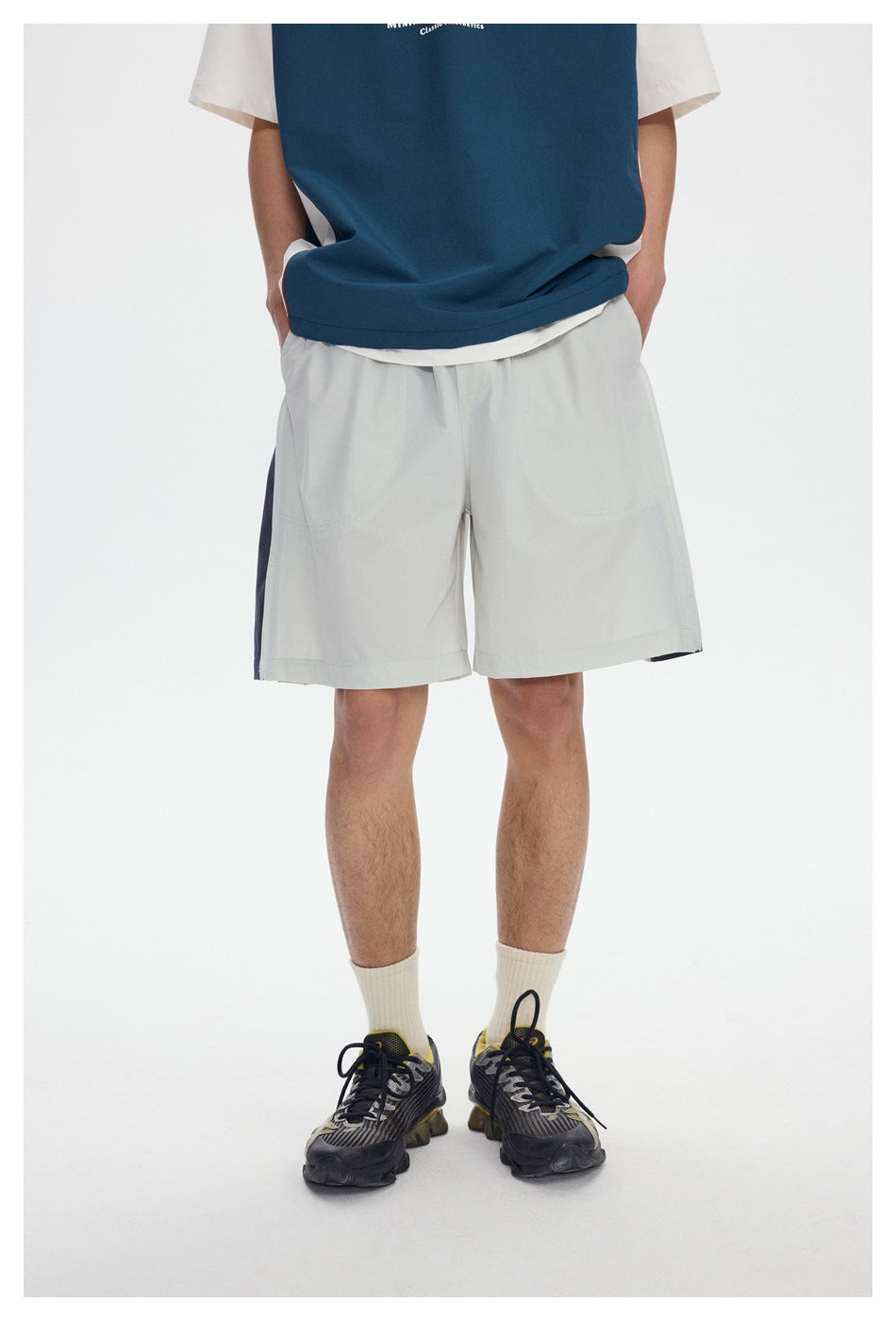 Front view of a model wearing light gray knee-length shorts with a blue tee and sneakers