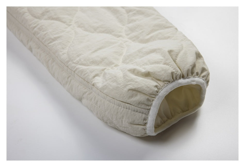 Close-up of an ivory quilted jacket sleeve ending in a rounded cuff with pale trim.