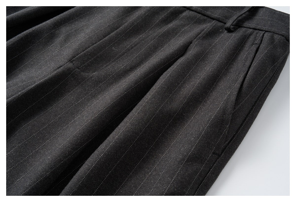 Close-up of charcoal pinstripe trousers showing a belt loop, waistband, and front pleat.