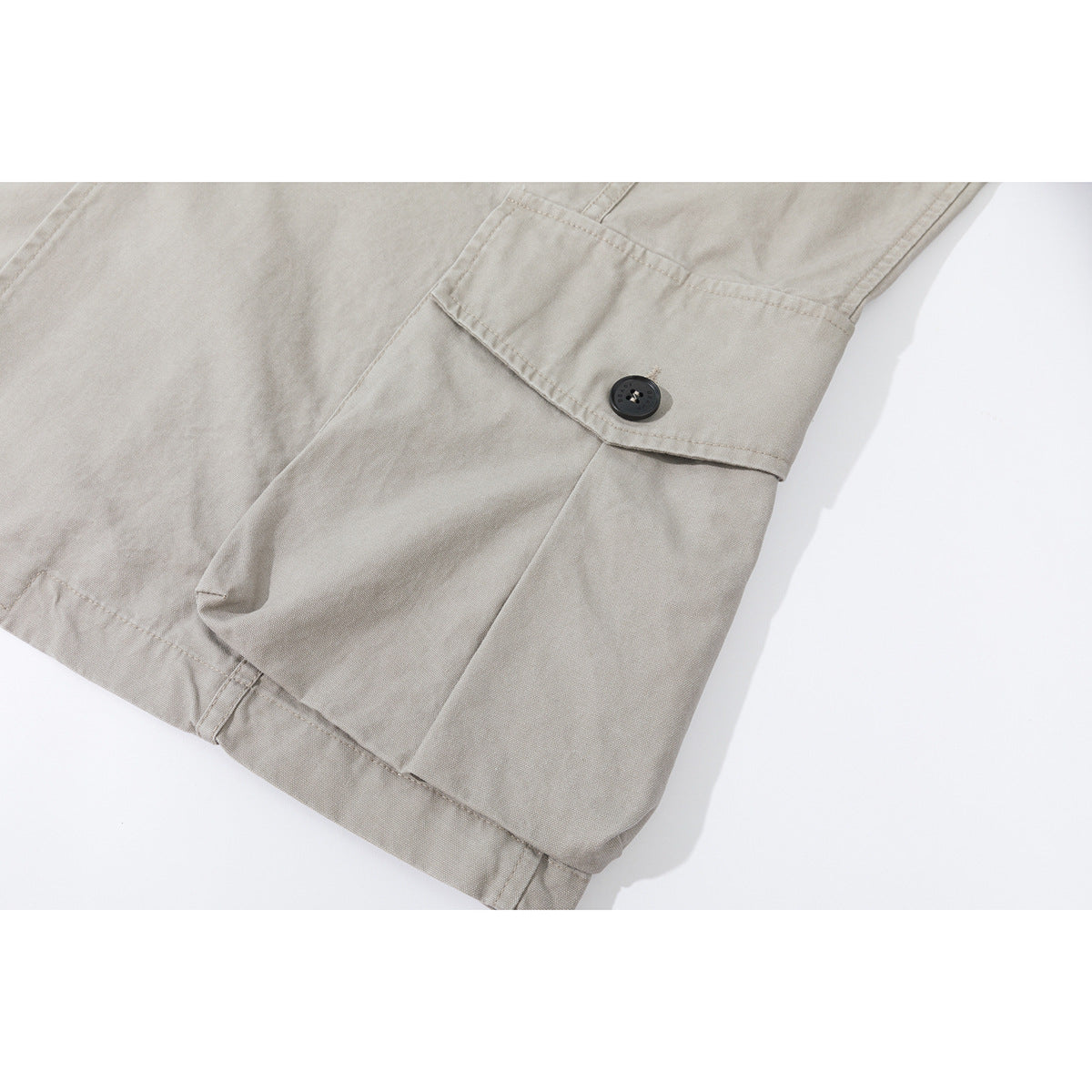 Close-up of a light gray-beige jacket pocket flap with a dark button and visible stitching.