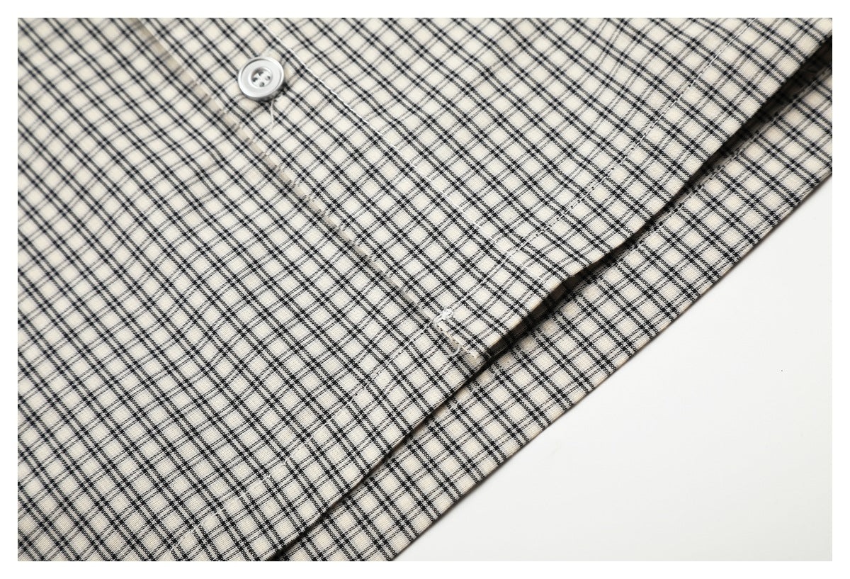 Close-up of a button and folded placket on a cream shirt with a black plaid pattern.