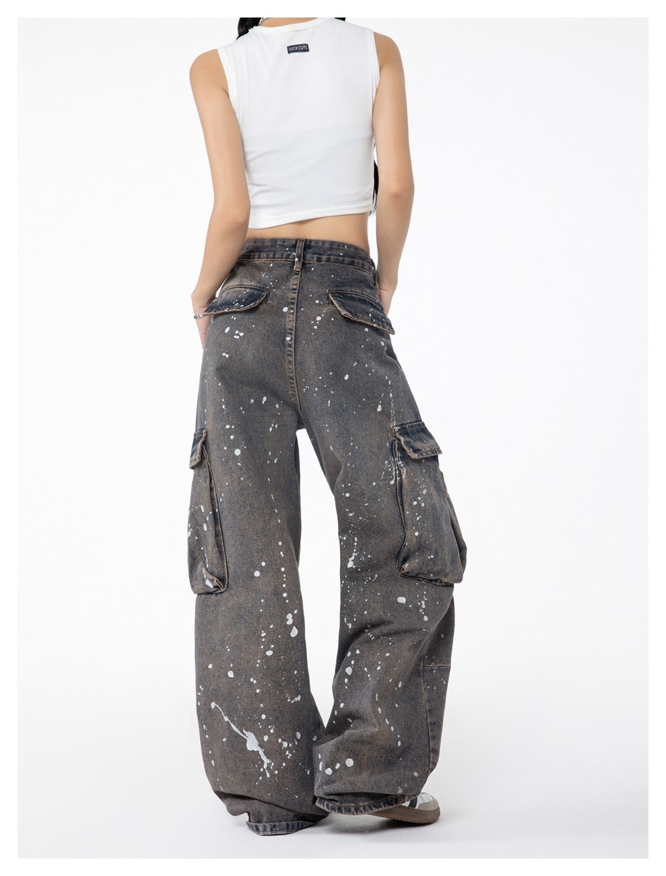 Angled back view of a model wearing loose charcoal-gray splatter-print cargo jeans with rear and side flap pockets.