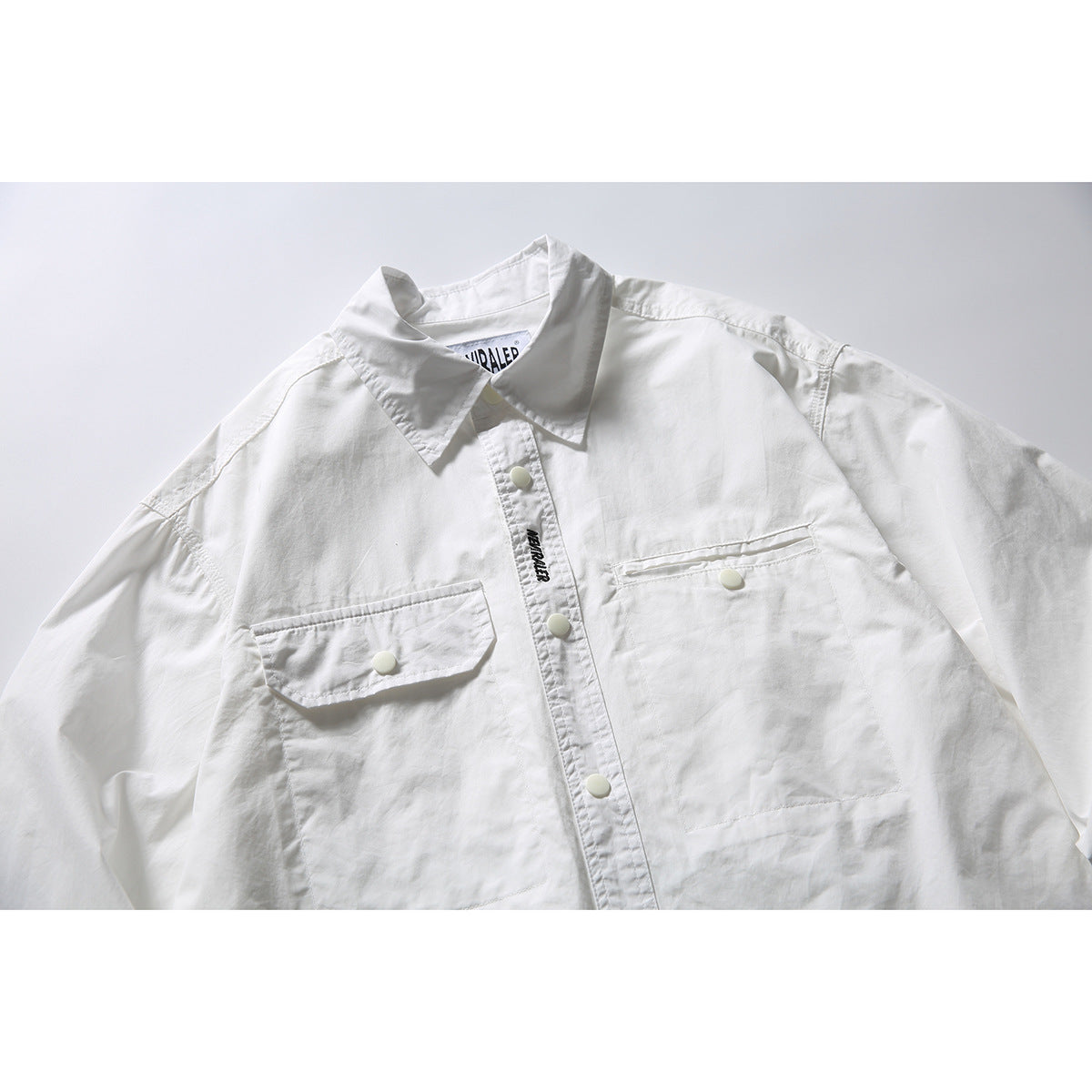 Close view of a white long-sleeve button-up shirt with a pointed collar, two chest pockets and snap buttons.