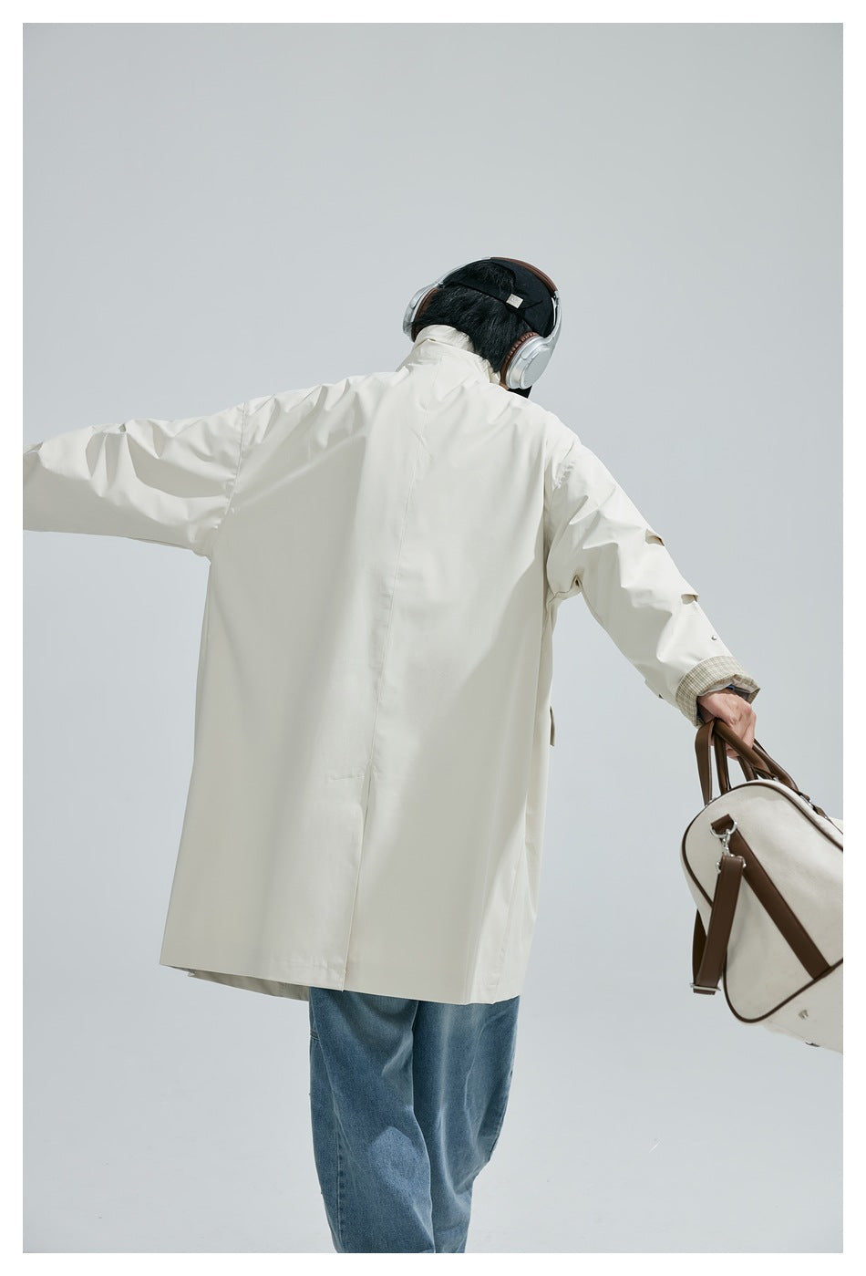 Rear view of a person wearing a long ivory coat with a high collar and plaid cuffs, paired with blue jeans.