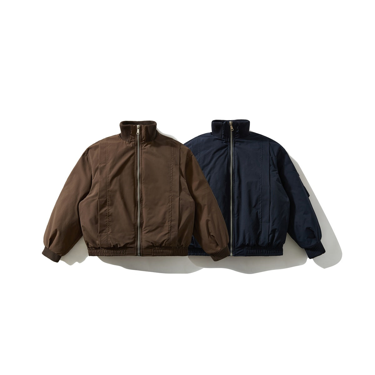 Front view of two zip-up jackets with ribbed collars and cuffs, in brown and navy.