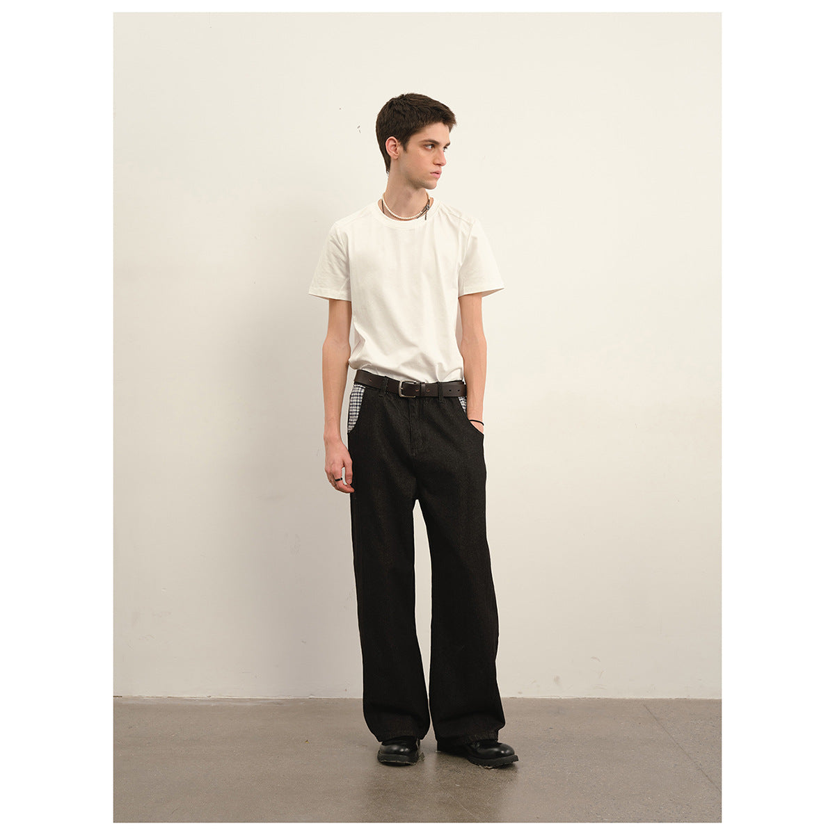 Model wearing a plain white T-shirt tucked into wide-leg black trousers with checked pocket accents.