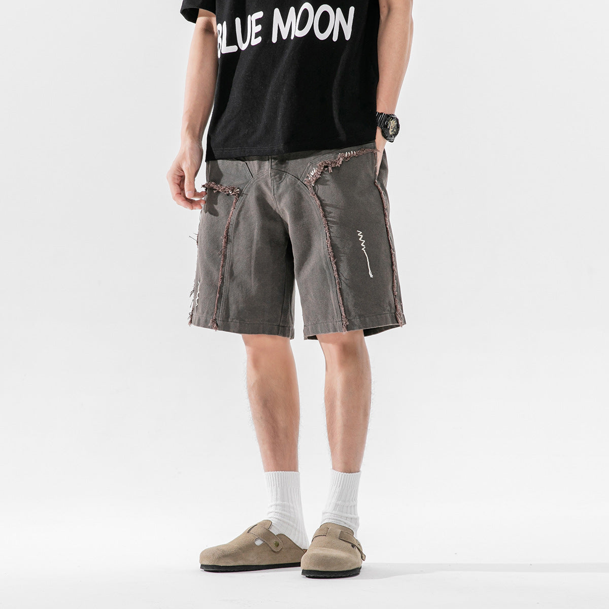 Model wearing charcoal shorts with frayed panel seams; a black T-shirt has white BLUE MOON lettering.