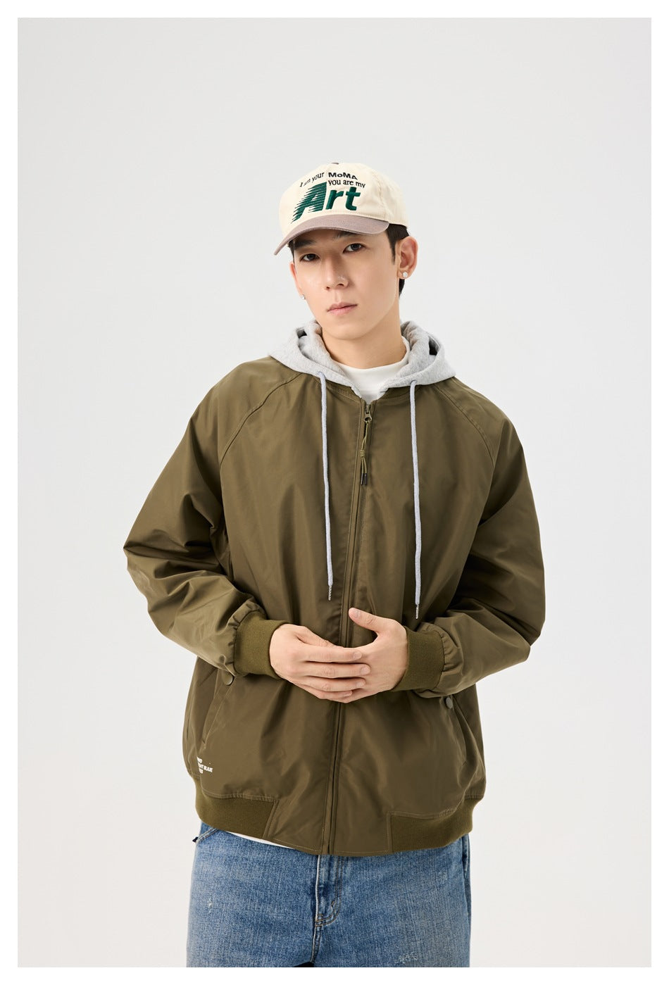 Front view of a model wearing an olive hooded zip jacket with gray drawstrings and ribbed trim.