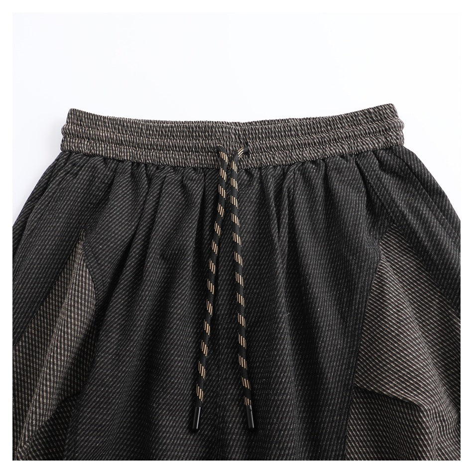 Cropped view of dark striped pants showing the elastic waistband, accented drawstring, and angled pocket panels.