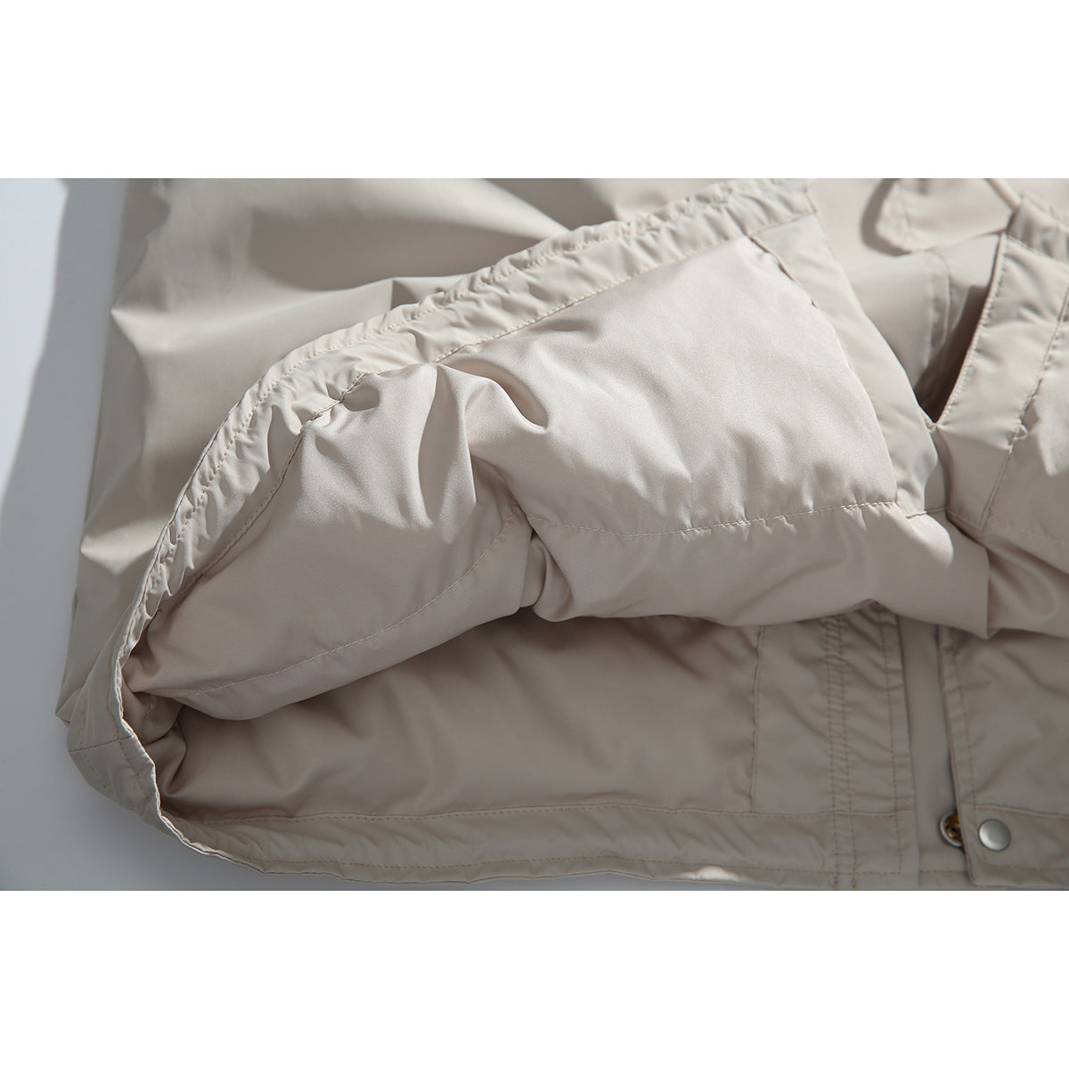 Close-up of a light beige coat sleeve and cuff, showing the lining, stitching, and snap-fastened front.