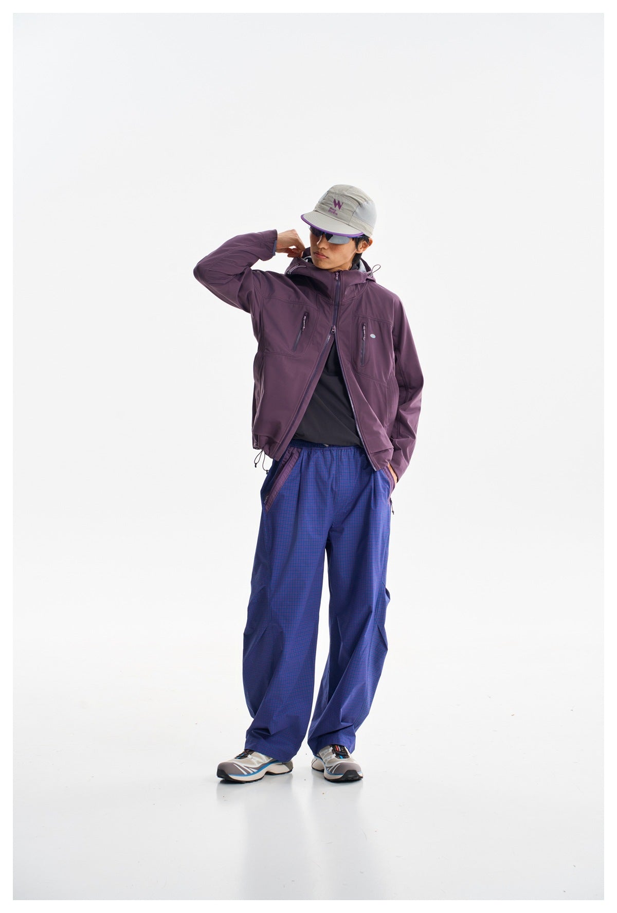 Model wearing a plum hooded jacket open over a dark top with loose blue checked trousers.