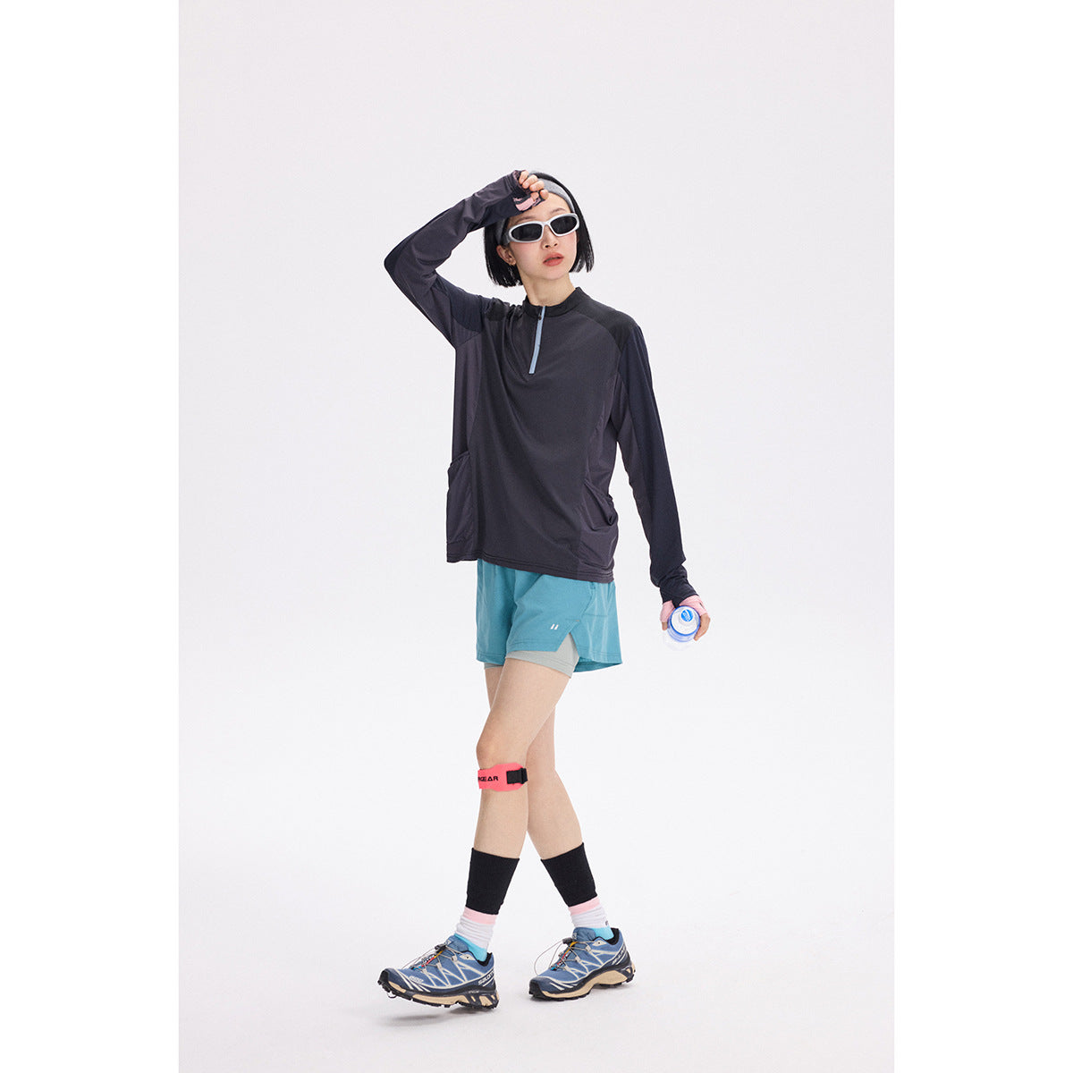 Woman wearing a charcoal long-sleeve quarter-zip top and turquoise running shorts.