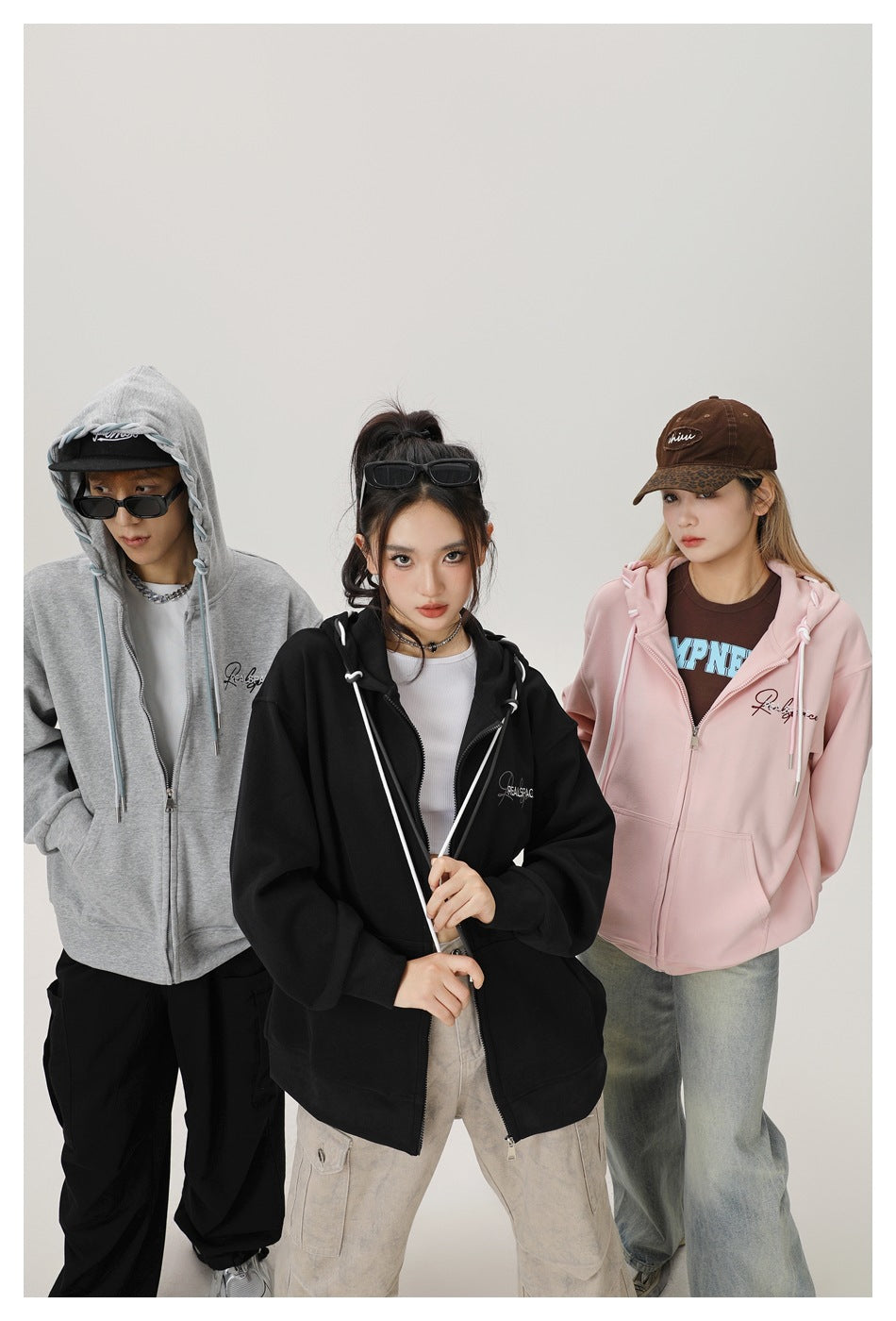 Three models wearing gray, black and pink zip hoodies, with the gray hood up, close studio shot