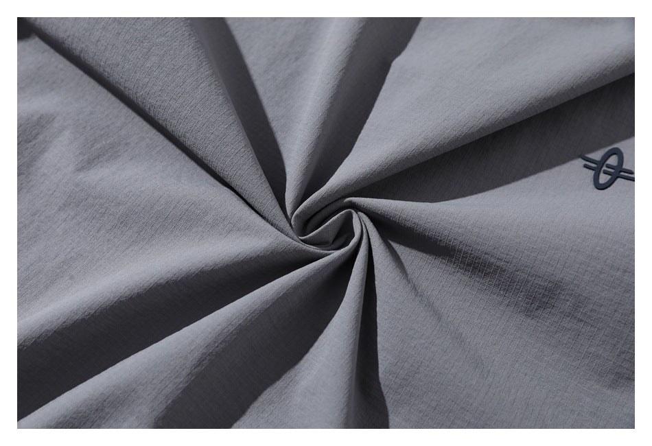 Close-up of gray fabric gathered into folds, with a small dark emblem near the edge.