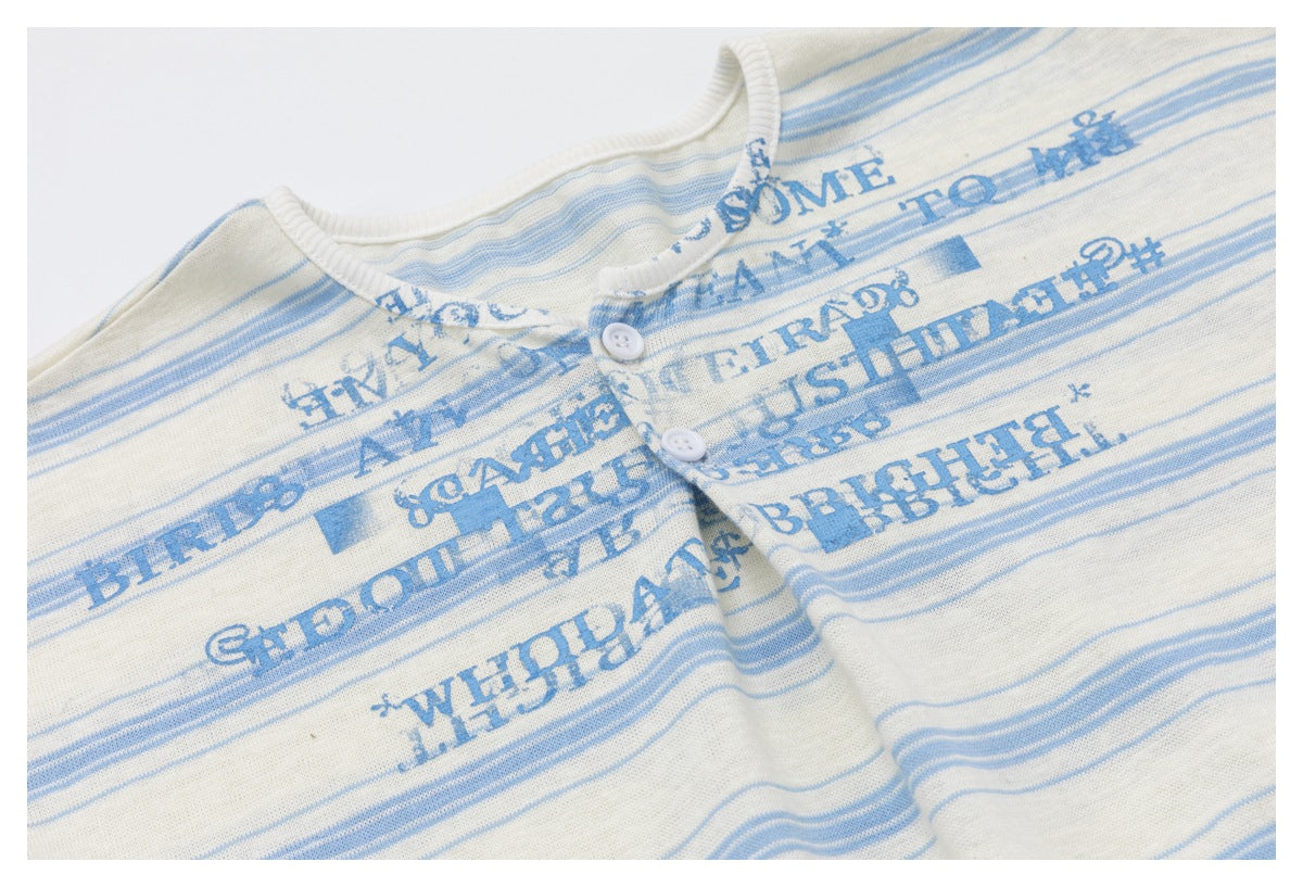 Close-up of blue text print and thin stripes on the cream top, with two white buttons at the neckline.