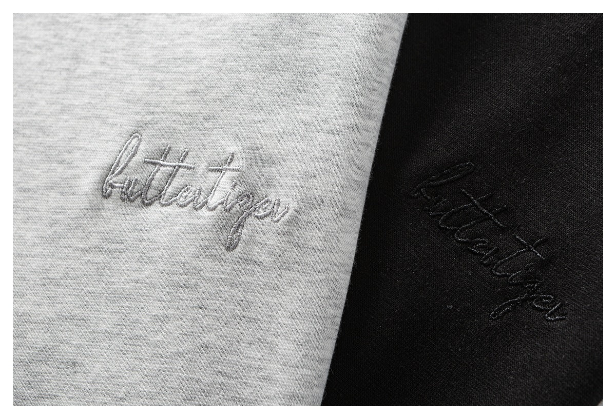 Close-up of cursive embroidery on light gray and black knit fabric.