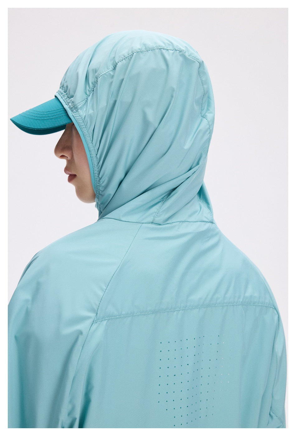 Close side view of a pale aqua jacket's hood over a teal cap, with dotted detailing on the back.