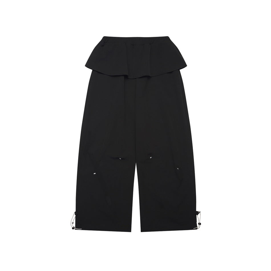Black wide-leg pants with a flounce waist panel and hem drawcords, flat lay