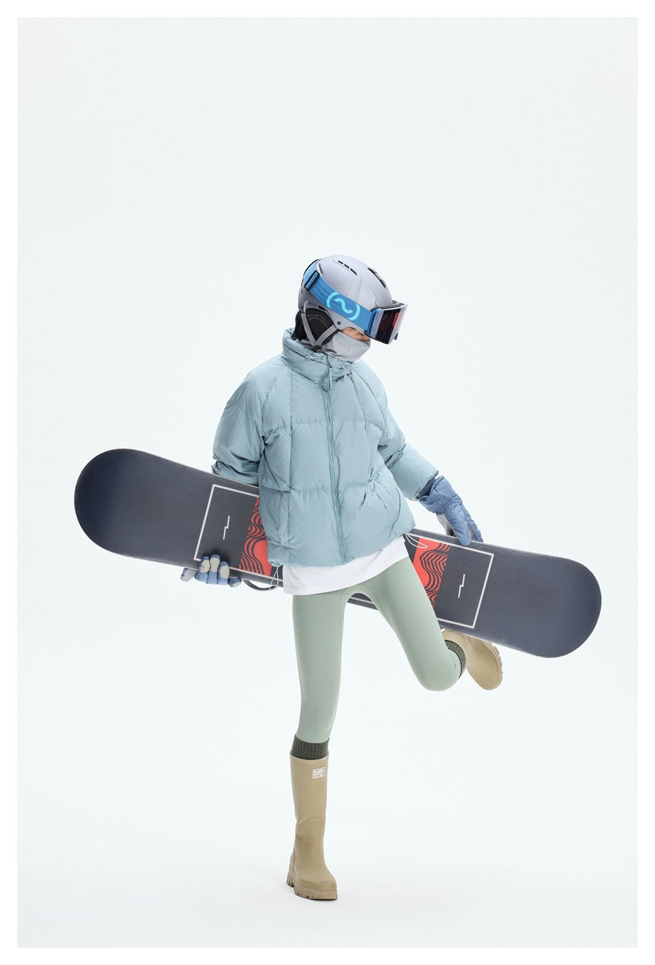 Person in a pale blue puffer jacket and ski gear posing with a snowboard held across their body.