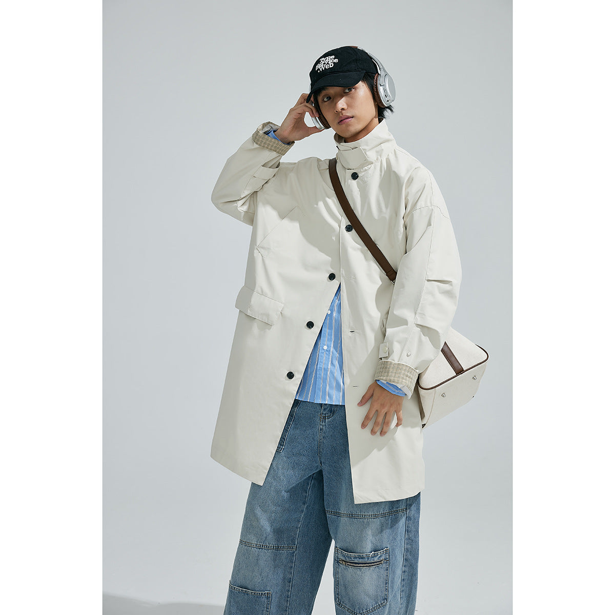 Model wearing a cream long coat with black buttons and plaid cuffs, shown from the front.