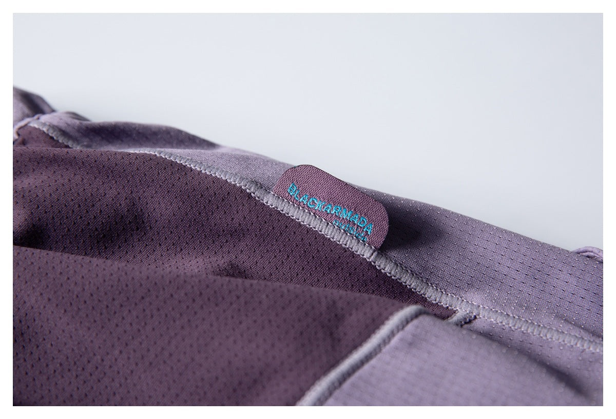 Close-up of a sewn BLACKMAMBA label on purple perforated garment fabric.