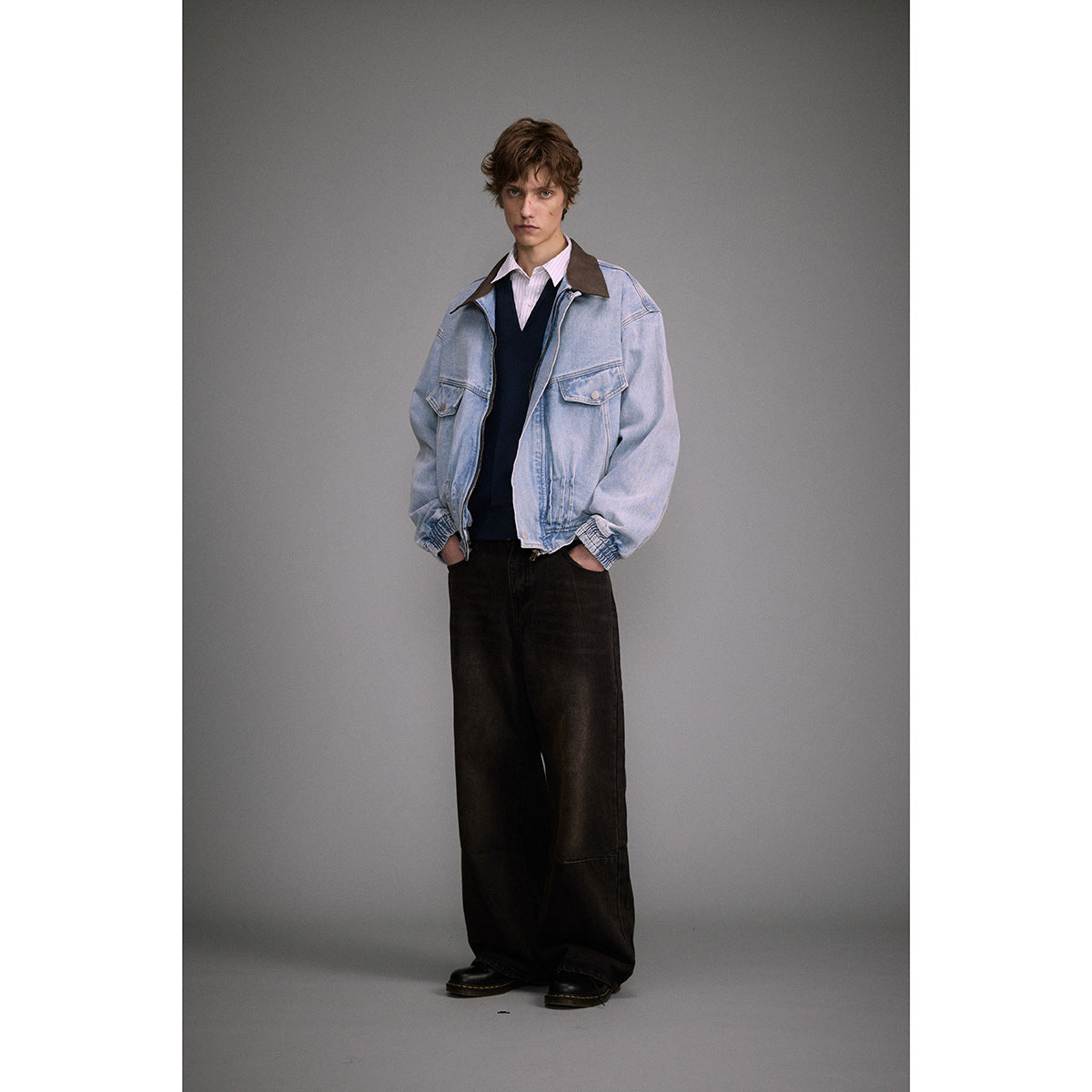 Model wearing an oversized light blue denim jacket with a brown collar, layered over a shirt and dark sweater.