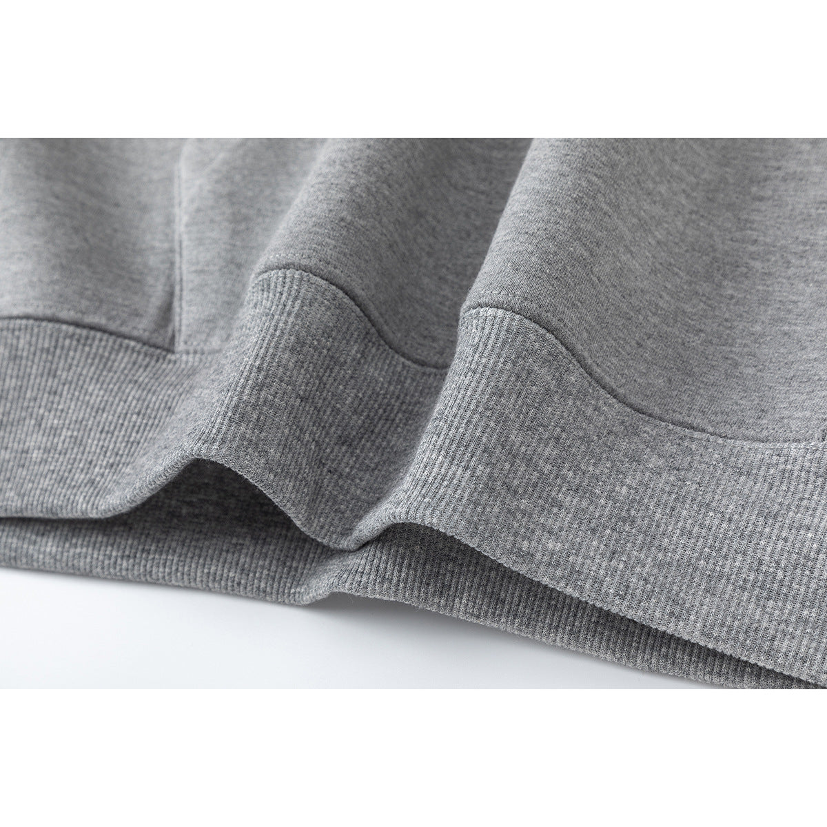 Close-up of the gray hoodie’s ribbed waistband and stitched hem.