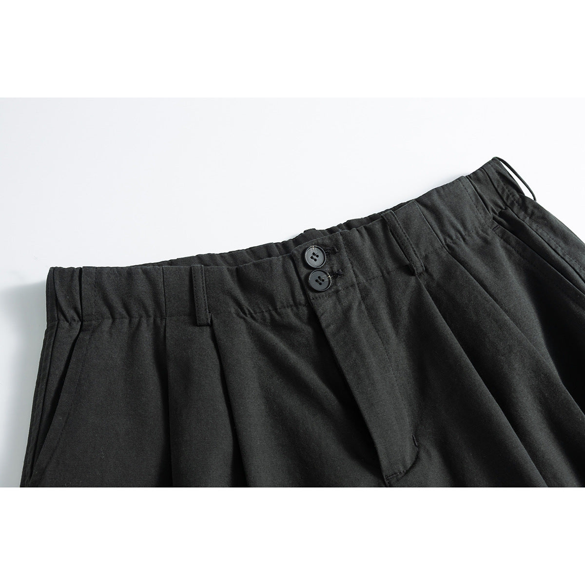 Close-up of charcoal trousers showing the pleated waistband, belt loops, two-button closure and front fly.