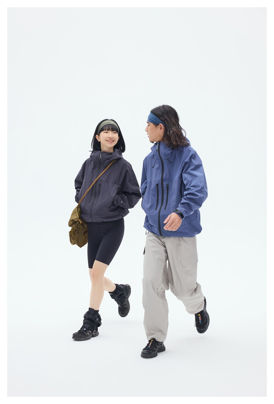 Two models walk together wearing charcoal and blue hooded jackets with zip pockets.
