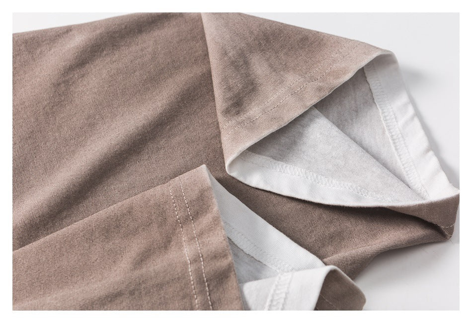 Close-up of a taupe T-shirt turned to show its white inner seams and stitched construction.