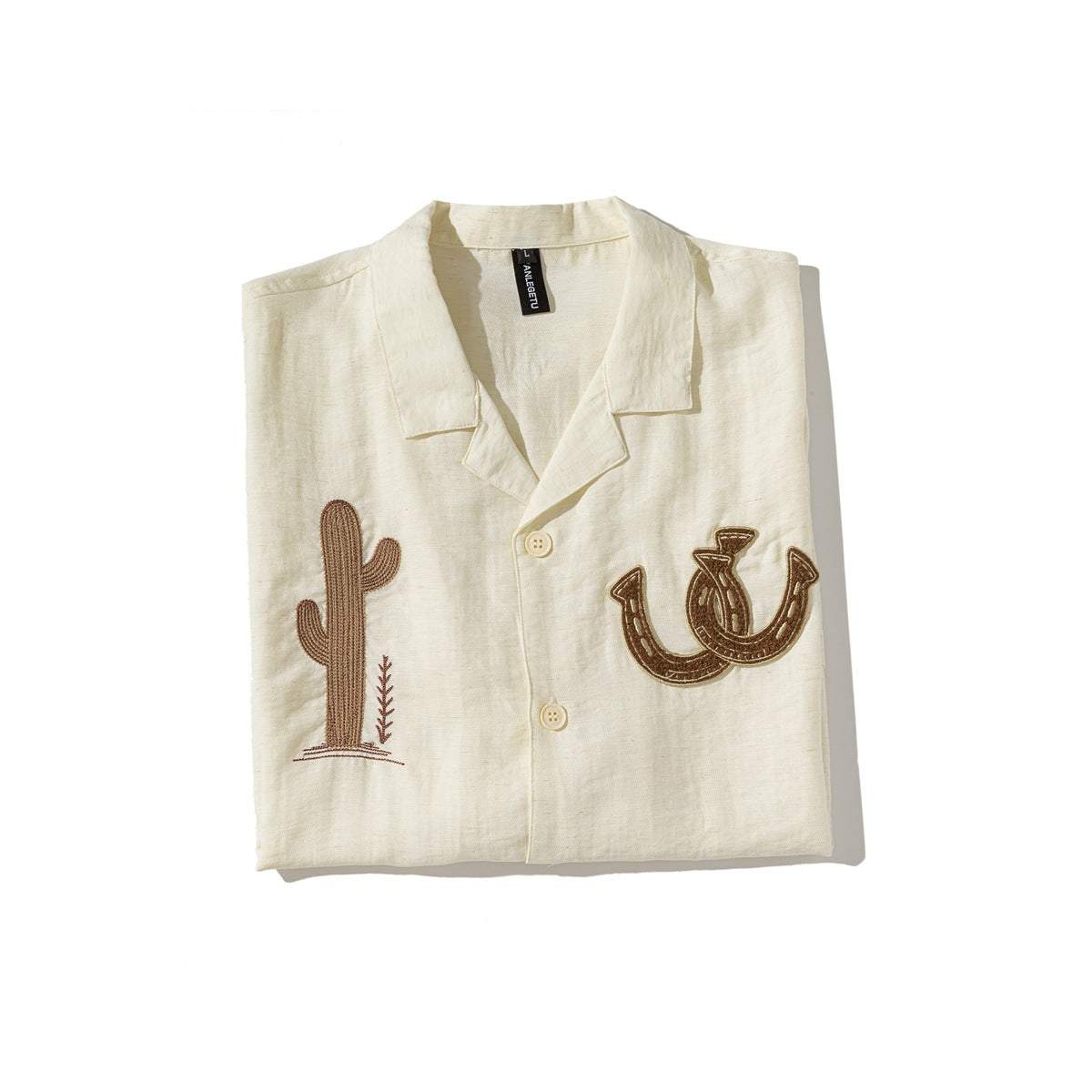 Folded ivory collared shirt with buttons and brown cactus and horseshoe embroidery on the front.