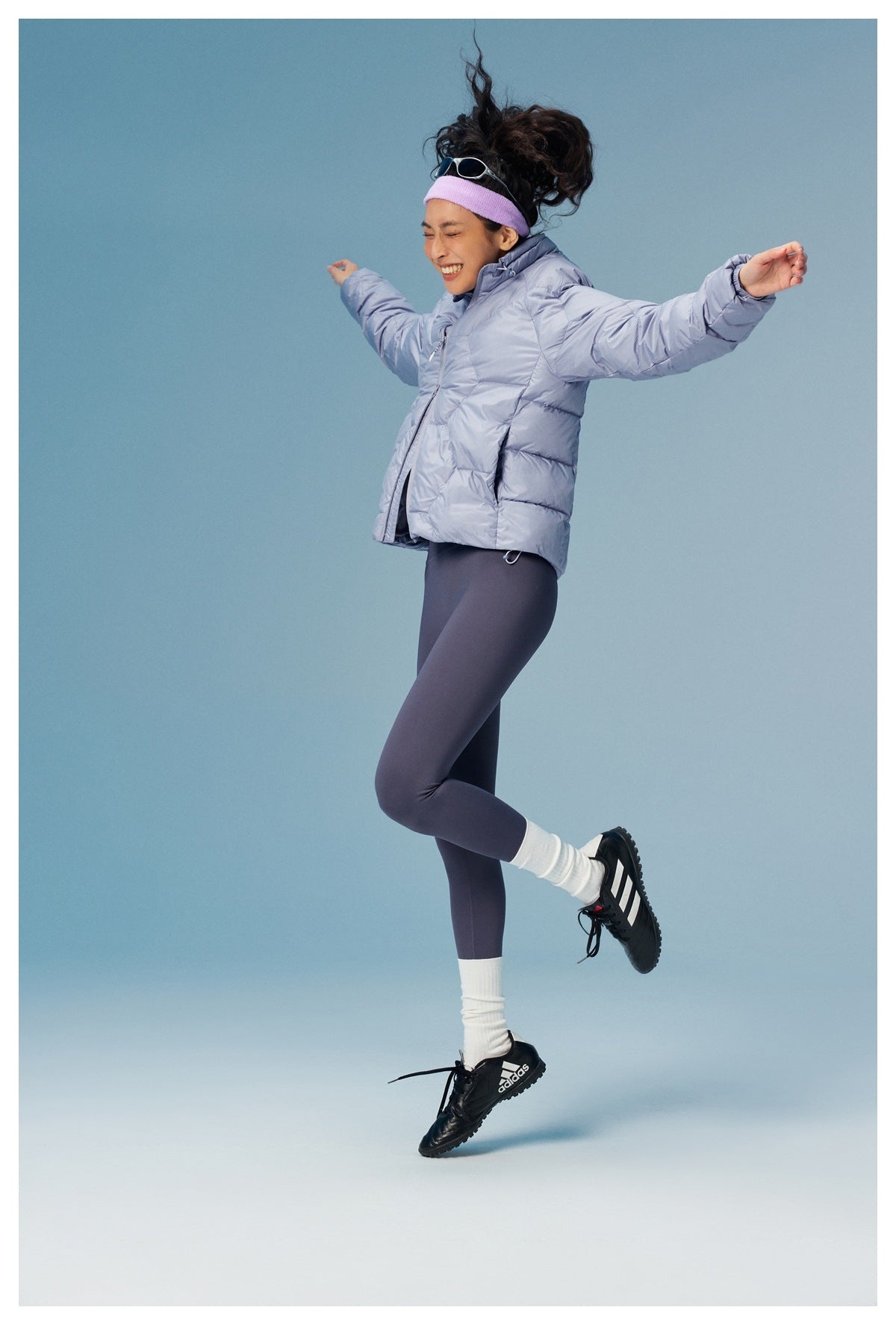 Model wearing a pale lavender quilted jacket and dark leggings, captured mid-jump with arms outstretched.