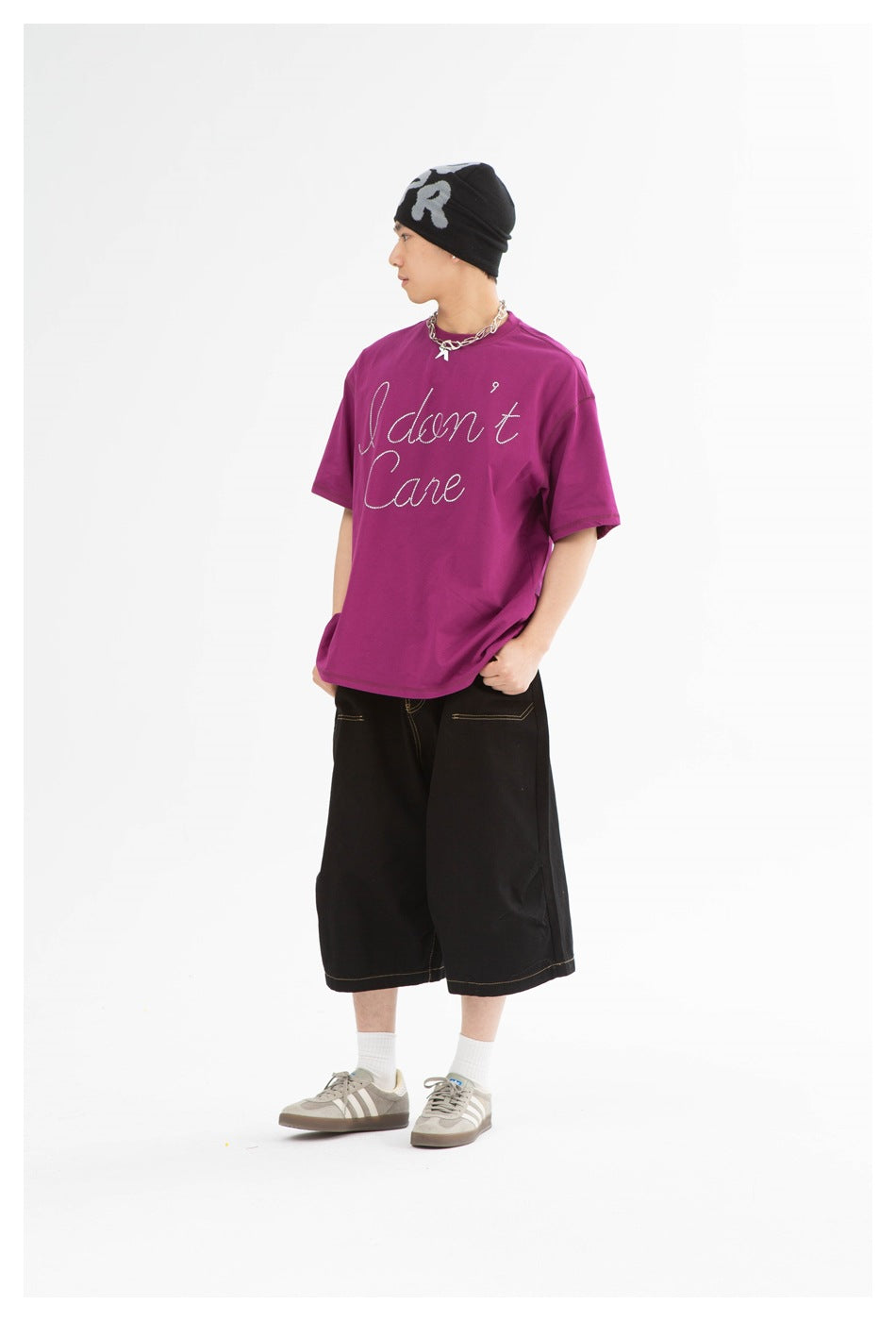 Model in a purple oversized 'I don't Care' T-shirt, black wide-leg shorts, beanie and sneakers, shown from the side