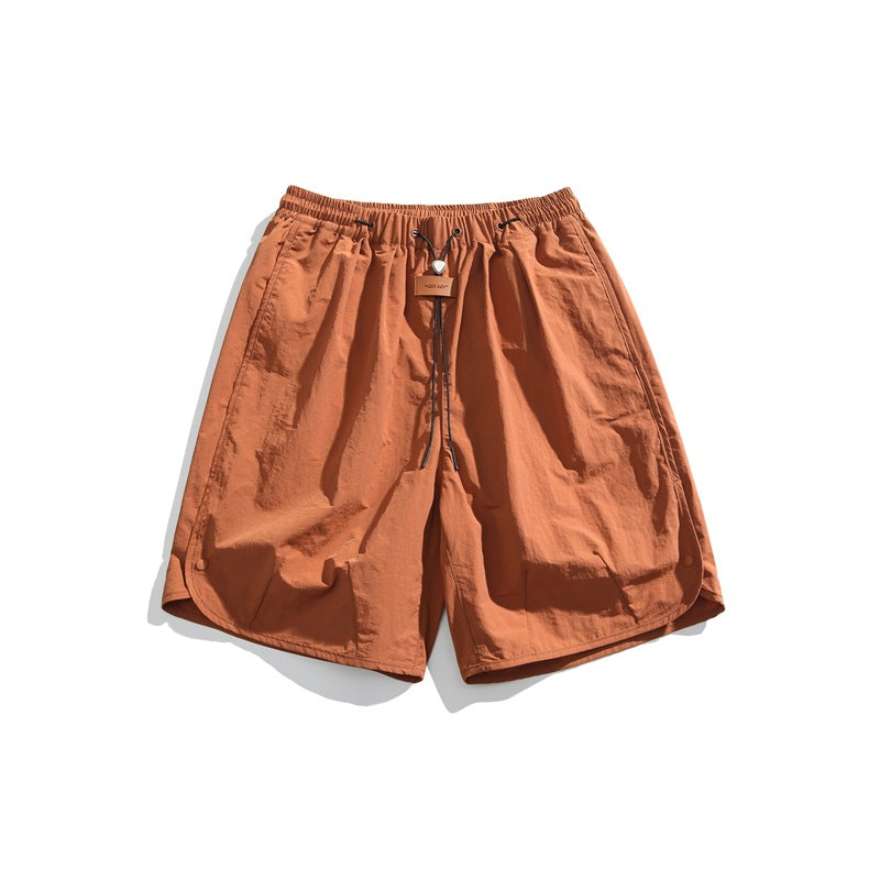 Rust orange knee-length shorts with elastic drawcord waist, leather-look tag and curved side hems, flat lay