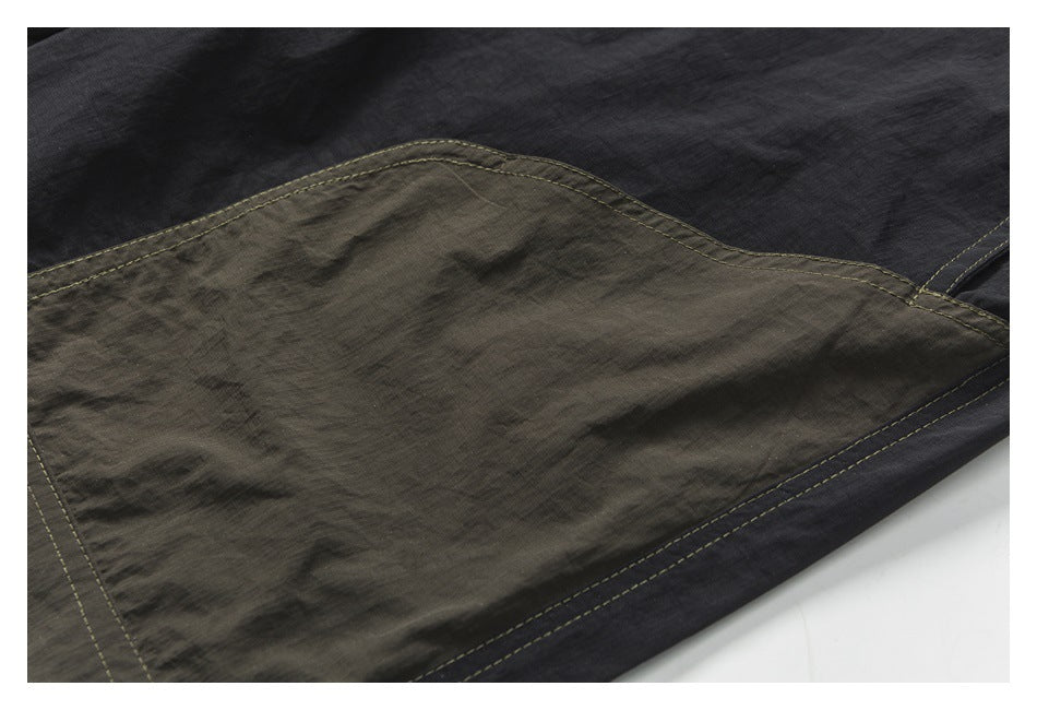 Close-up of a dark charcoal garment with a large olive-gray patch pocket and contrast stitching.
