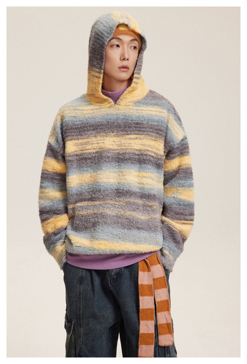 Model wearing the gray and yellow striped hooded knit sweater with the hood up, over a purple top