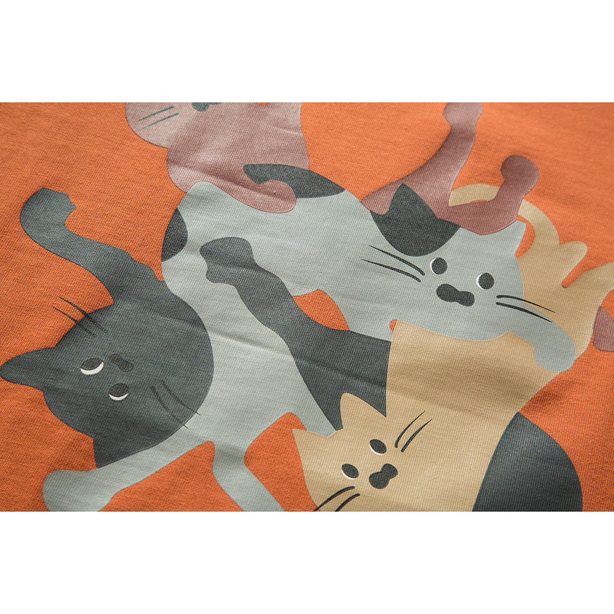 Close-up of a colorful print of several cats on orange T-shirt fabric.