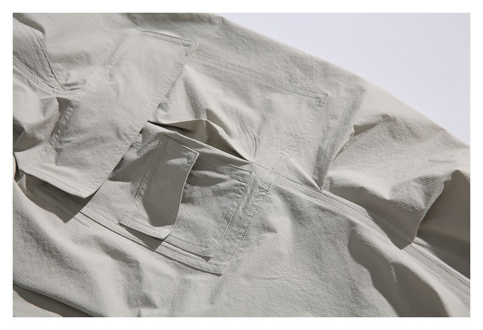 Close-up of a light gray garment showing layered stitched pocket flaps and a rectangular patch pocket.