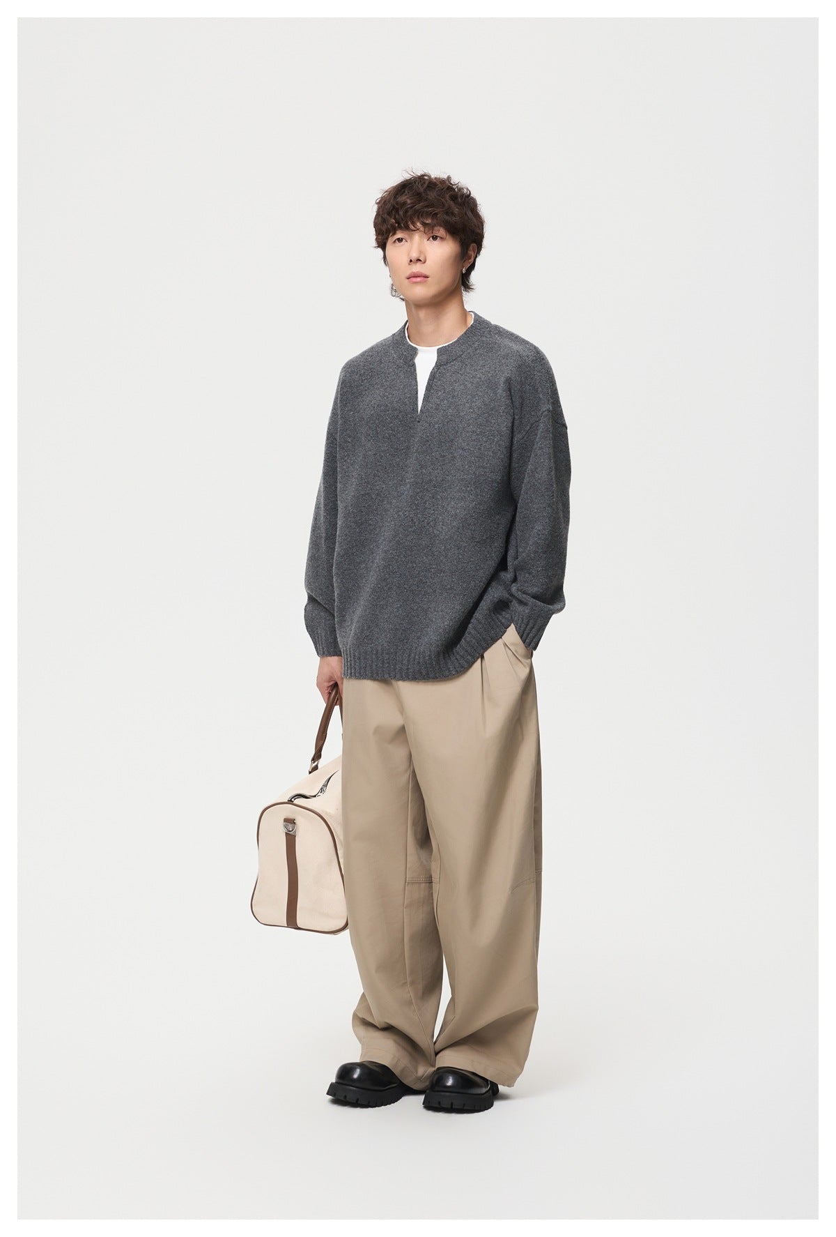 Full-length model wearing a charcoal gray sweater with a split crew neckline and loose beige trousers.