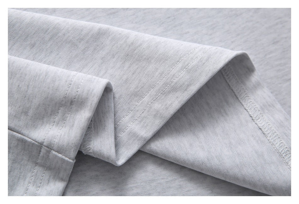 Close-up of folded light gray heathered fabric showing the garment's hem stitching and overlocked seam.