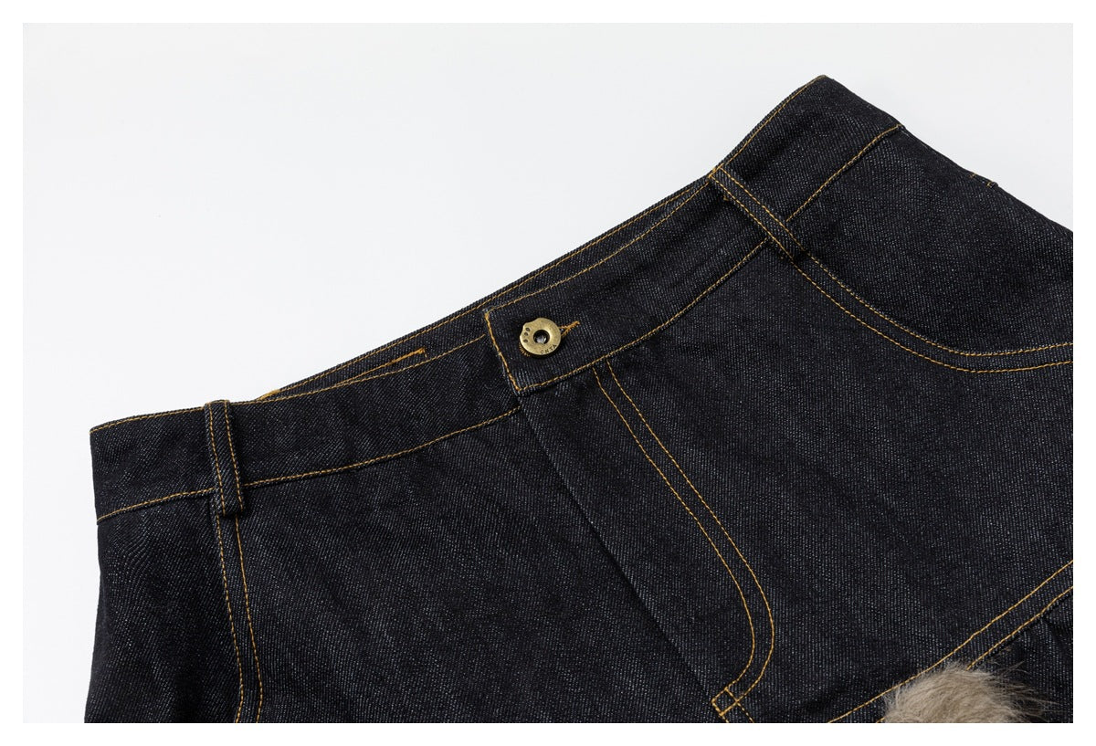 Angled close-up of dark indigo jeans showing the waistband, belt loop, button and fly stitching.